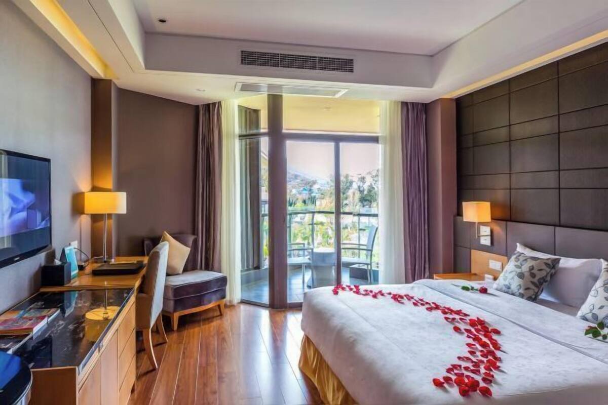 Una habitación de hotel con cama, escritorio, televisión y balcón con mobiliario exterior.
