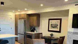 A modern kitchen with a dining area, bar stools, and a fireplace. - The Suite at Sunset Point (Ucluelet)