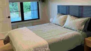 A bedroom with a bed, a window, and a plant. - The Suite at Sunset Point (Ucluelet)