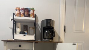Un espace cuisine compact comprenant un coin café, avec une machine à café, des dosettes de café et un mixeur.