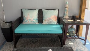 Un canapé en osier avec des coussins turquoise, une table basse en verre ornée d’une sculpture de tortue et des œuvres d’art encadrées accrochées au mur.
