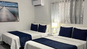 Une chambre d’hôtel avec deux lits, un ventilateur de plafond, un appareil de climatisation, un tableau au mur et une fenêtre avec des rideaux.