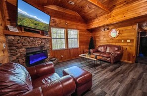 L’intérieur chaleureux d’un chalet avec une cheminée en pierre, des meubles en cuir et un téléviseur fixé au mur.
