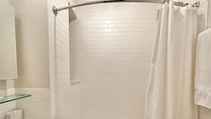 Une salle de bain moderne avec des carreaux de céramique blancs rectangulaires, une étagère en verre, une baignoire et un rideau de douche.