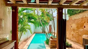 A room with a pool, wooden ceiling, and a view of a garden with palm trees. - Paseo Colonial - Leo's Favorite (Santo Domingo)