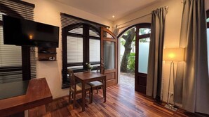 A room with a wooden floor, a dining table with chairs, a flat-screen TV mounted on the wall, and a large window with blinds. - Paseo Colonial - Leo's Favorite (Santo Domingo)