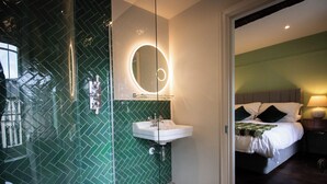 A modern bathroom with a green herringbone tile backsplash, a white sink, and a round mirror with a light. - Y Castell  (Llangadog)