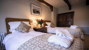 Een hotelkamer met twee bedden, elk met een beddekleed met dessin, kussens en opgevouwen handdoeken. Er staat een nachtkastje met een lamp en een bloemenvaas. Een houten kledingkast is op de achtergrond te zien.