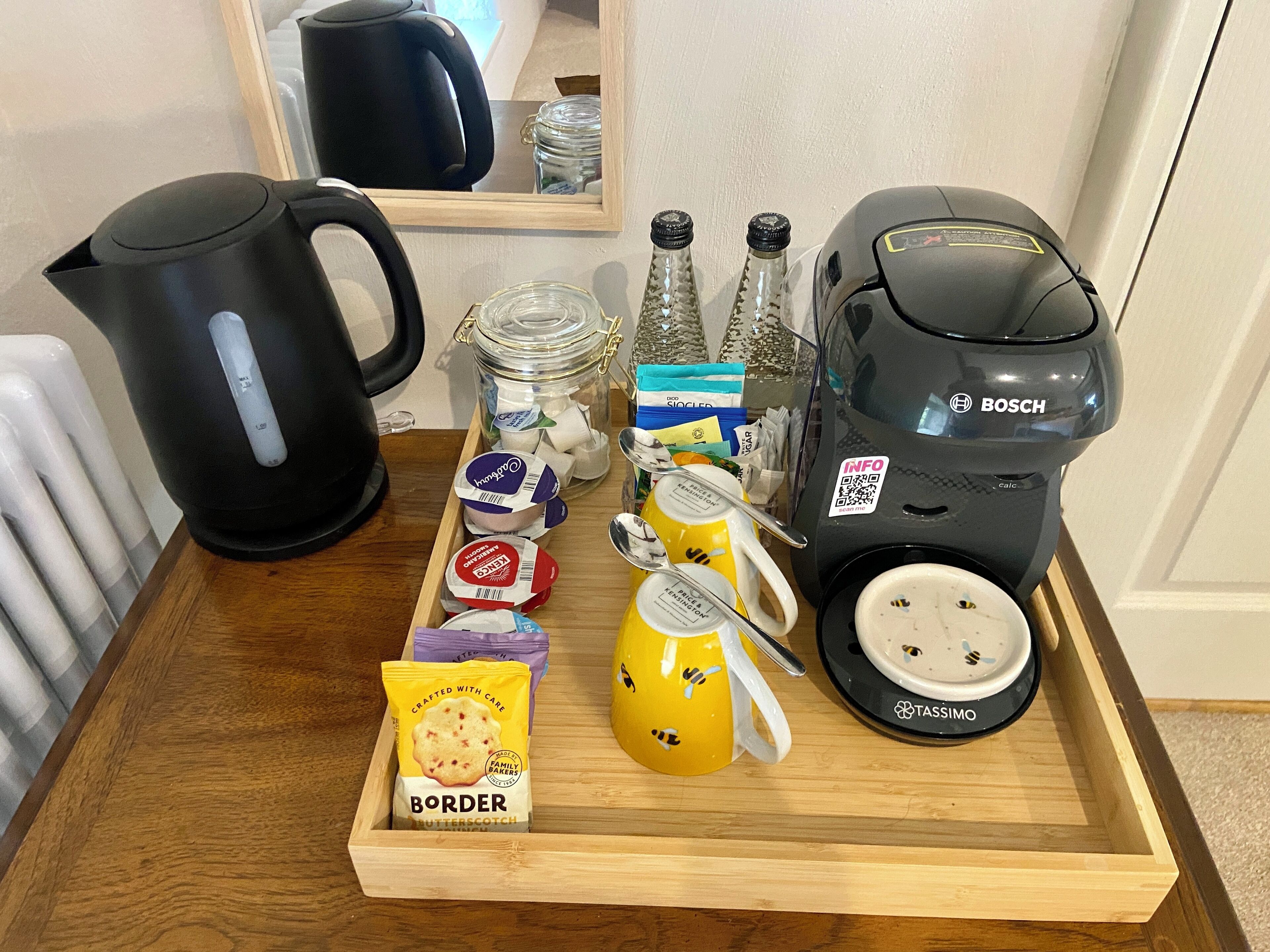 Ein Holztablett mit einer Kaffeemaschine, einem Wasserkocher, Gläsern, einer Tasse und verpackten Snacks.