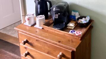 A wooden cabinet with drawers, a coffee maker, a kettle, and a cup on top.