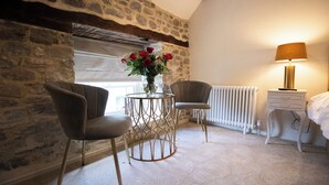 A cozy room with a stone wall, a round table with a vase of flowers, two chairs, a radiator, and a bedside table with a lamp. - Y Castell  (Llangadog)