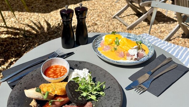 A table set outdoors with plates of food, including eggs, bacon, and beans, and two salt shakers. - Y Castell  (Llangadog)