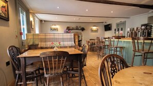 A dining area with wooden tables and chairs, a bar with multiple taps, and a stone wall with a fireplace. - Y Castell  (Llangadog)
