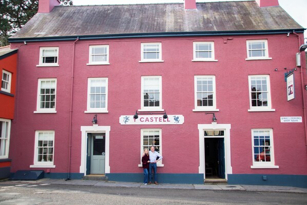A red building with a sign reading "CASTELL" and a door with a blue awning. - Y Castell  (Llangadog)
