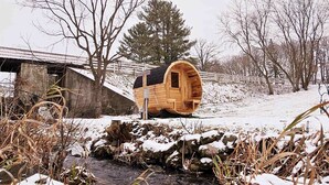 Eine Holzhütte mit geneigtem Dach, gelegen an einem Bach, bedeckt mit Schnee, umgeben von Bäumen.
