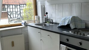A modern kitchen with white cabinets, a black countertop, a window with a view of houses, a built-in oven, and a radiator.