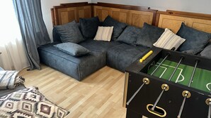 A living room with a sectional sofa, a foosball table, and a patterned throw pillow.