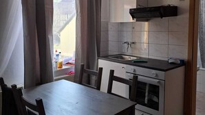 A compact kitchen with a dining table and chairs, a built-in oven, and a window with curtains.
