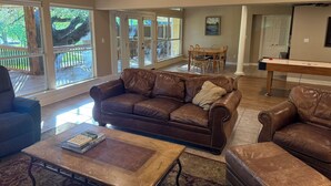 A spacious living room with a brown leather sofa, a coffee table, and a dining area with a wooden table and chairs. - Dog-Friendly Lakehouse: Dock + Serene Views (Burnet)