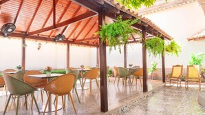 A covered outdoor dining area with tables and chairs, a tiled floor, and hanging plants. - Hotel Galeria la Vieja Sara Riohacha (Riohacha)
