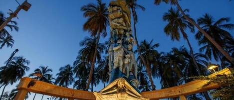 A tall, ornate statue with a figure at the top, surrounded by palm trees and a clear sky.