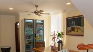 A dining area with a wooden table, benches, a refrigerator, and a ceiling fan. - Hotel Galeria la Vieja Sara Riohacha (Riohacha)