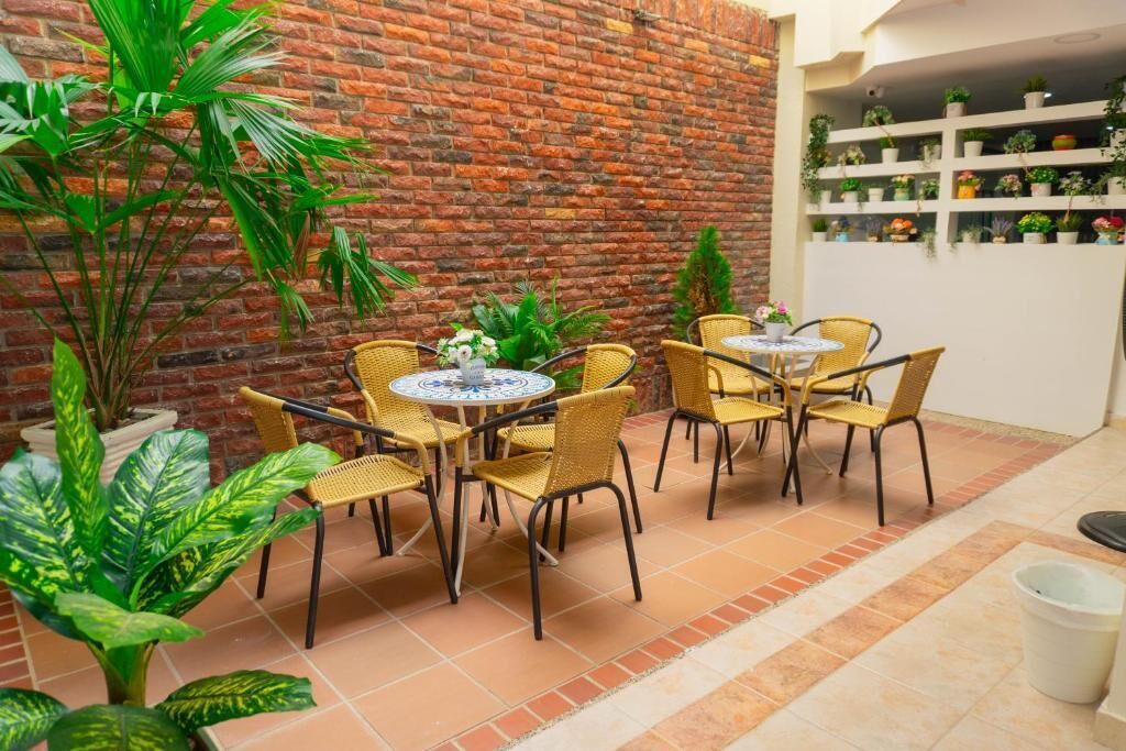 A patio area with wicker chairs and tables, surrounded by potted plants and a brick wall.
