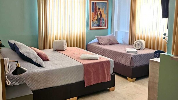 A hotel room with two beds, a painting on the wall, and a desk with a lamp. - Hotel Galeria la Vieja Sara Riohacha (Riohacha)