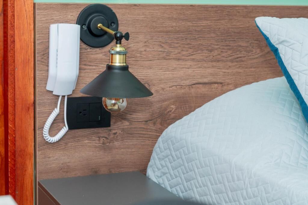 En sengegavl i træ med en telefon, en lampe og en stikkontakt.