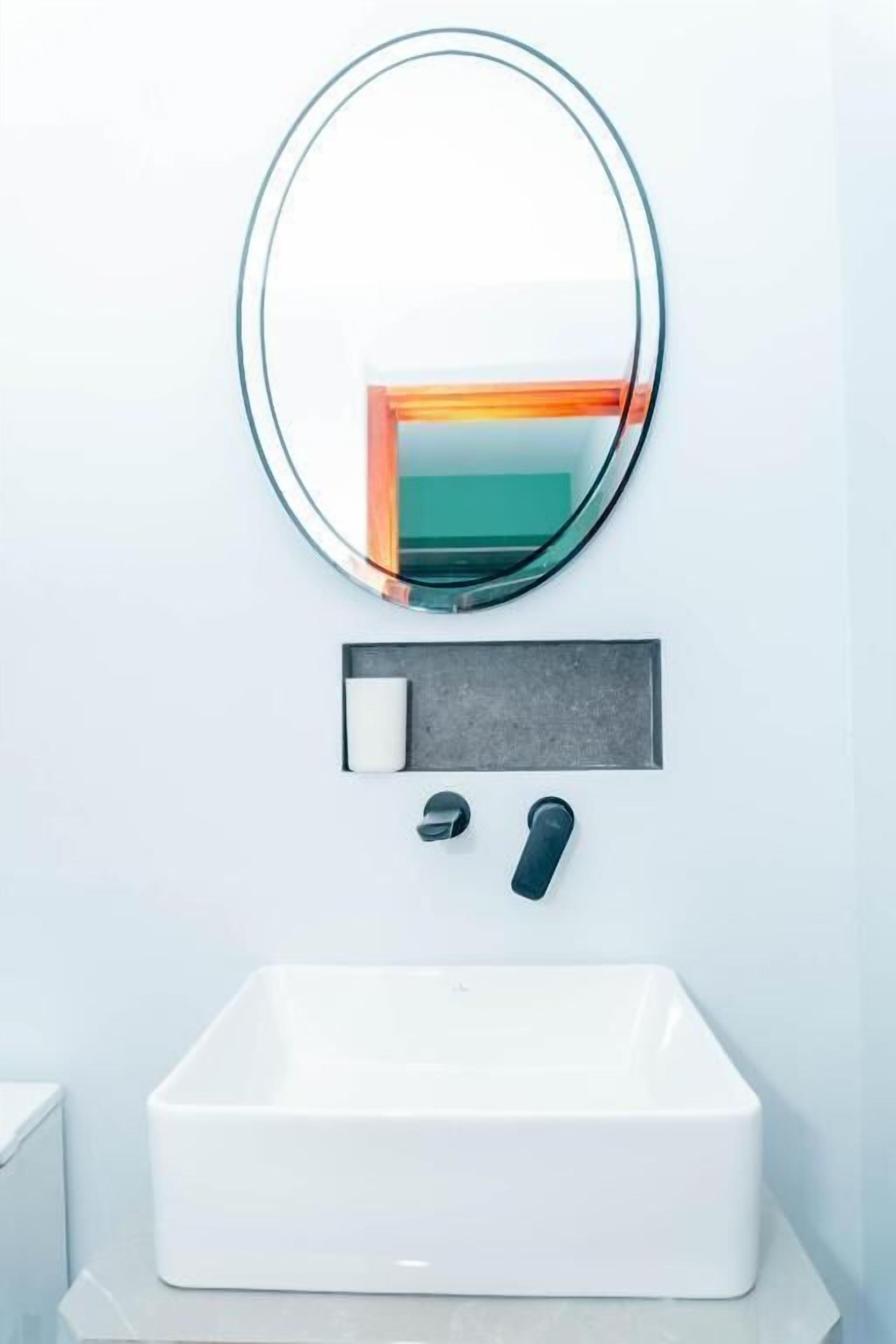 Un bagno moderno con un lavandino bianco, uno specchio rotondo e un erogatore di sapone.