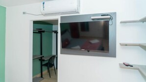 A room with a mounted TV, a small table, a chair, and a shelf with a remote control. - Hotel Galeria la Vieja Sara Riohacha (Riohacha)