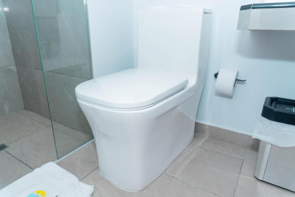 Un baño moderno con inodoro blanco, cabina de ducha con vidrio y dispensador de toallas de papel.