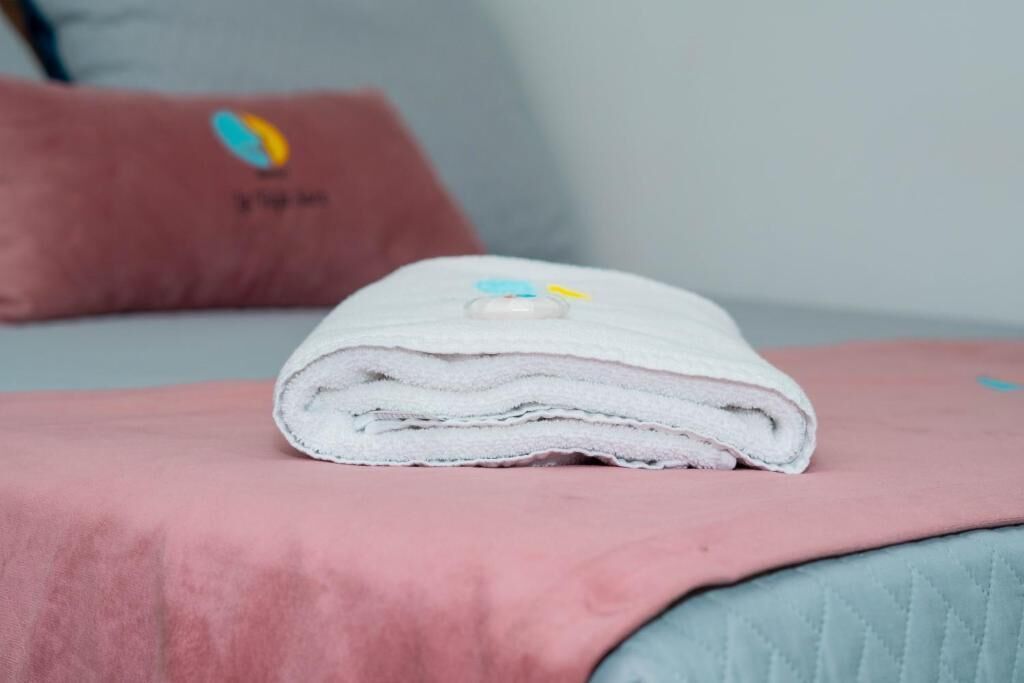 A neatly folded white towel on a pink bedspread with a pillow featuring a logo.
