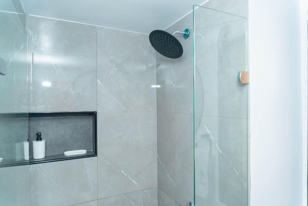 A modern bathroom with a glass-enclosed shower, marble walls, and a shelf with toiletries.