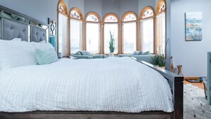 A modern bedroom with a large bed, a ceiling fan, and a view of the city through arched windows.