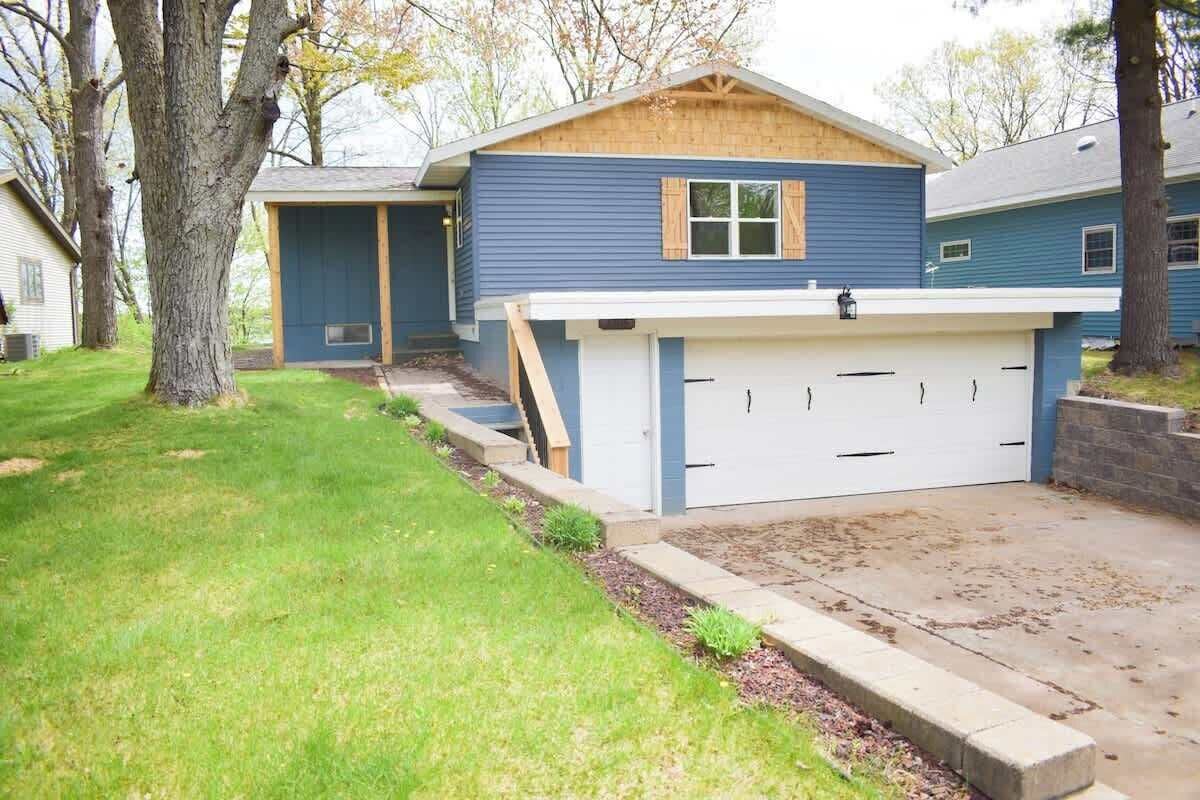 A residential house with a garage, a covered porch, and a well-maintained lawn.