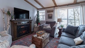 Ein gemütliches Wohnzimmer mit Kamin, Fernseher, Sofa und Seeblick.