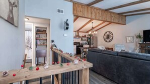 Ein modernes Wohnzimmer mit einer Holztreppe, einem grauen Sofa und einem Küchenbereich im Hintergrund.