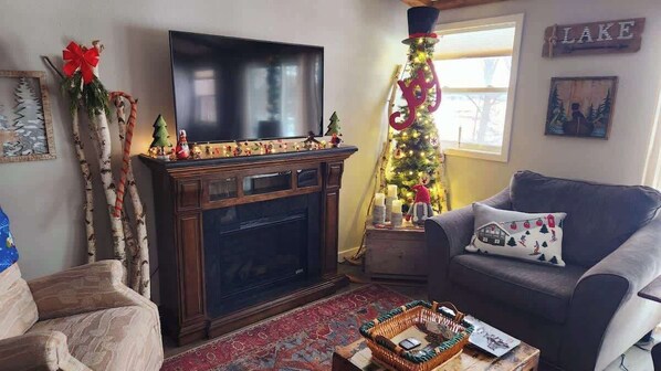 Un salon avec une cheminée, un téléviseur, un canapé et un sapin de Noël.