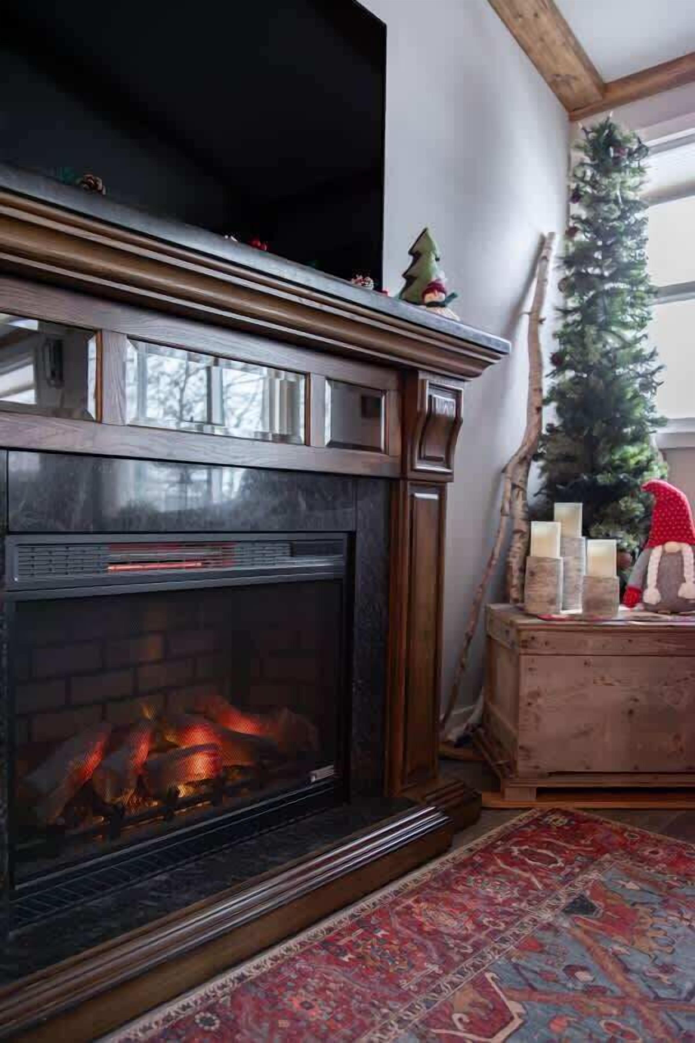 Una chimenea con fuego a la vista, un árbol de Navidad y un aparador de madera con velas.