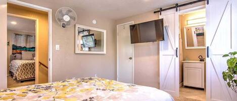 Un dormitorio con cama, televisor montado en la pared, armario con puerta corredera y ventilador.