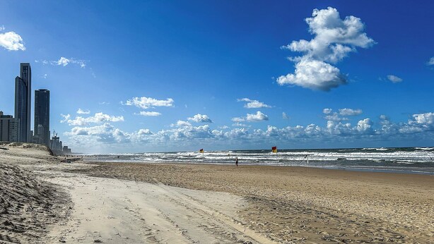 Une plage avec un rivage sablonneux, des vagues et un ciel bleu clair parsemé de nuages.