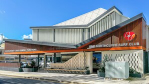 Un bâtiment moderne avec une enseigne indiquant « BMD Northcliffe Surf Club » et une zone couverte portant l’inscription « RESTAURANT - BAR - SALLE DE JEUX - ESPACE ÉVÉNEMENTIEL ».