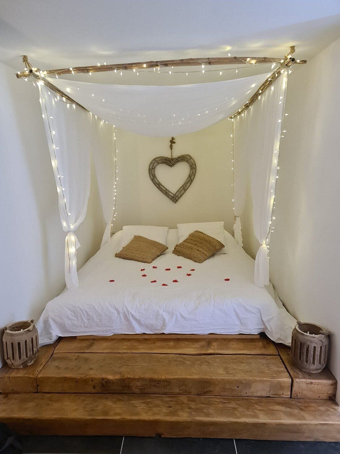 Una cama con dosel, decoración de corazón en la pared y pétalos de rosa sobre la cama.