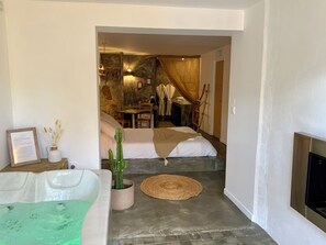 A modern hotel room with a stone wall, a bed, a small table, and a fireplace. - La Perle du Voyageur (Agde)