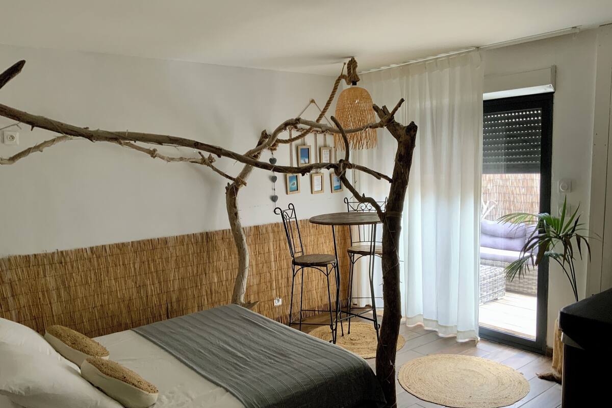 Une chambre avec un lit, une petite table, des chaises, une branche suspendue et une vue sur l’extérieur.