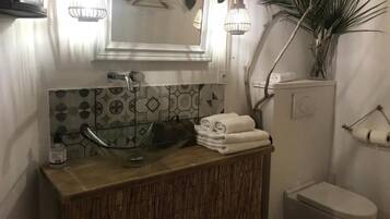 A bathroom with a glass sink, a mirror, a toilet, and a towel rack.