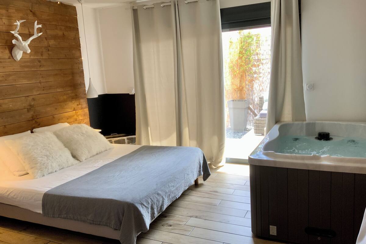 Une chambre avec un lit, une tête de lit en bois, un téléviseur, un jacuzzi et une vue sur l’extérieur.