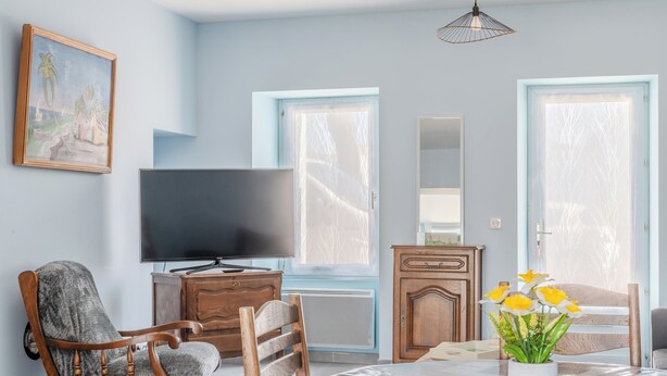 A living room with a television, a wooden chair, a dining table with a vase of flowers, and a cabinet.