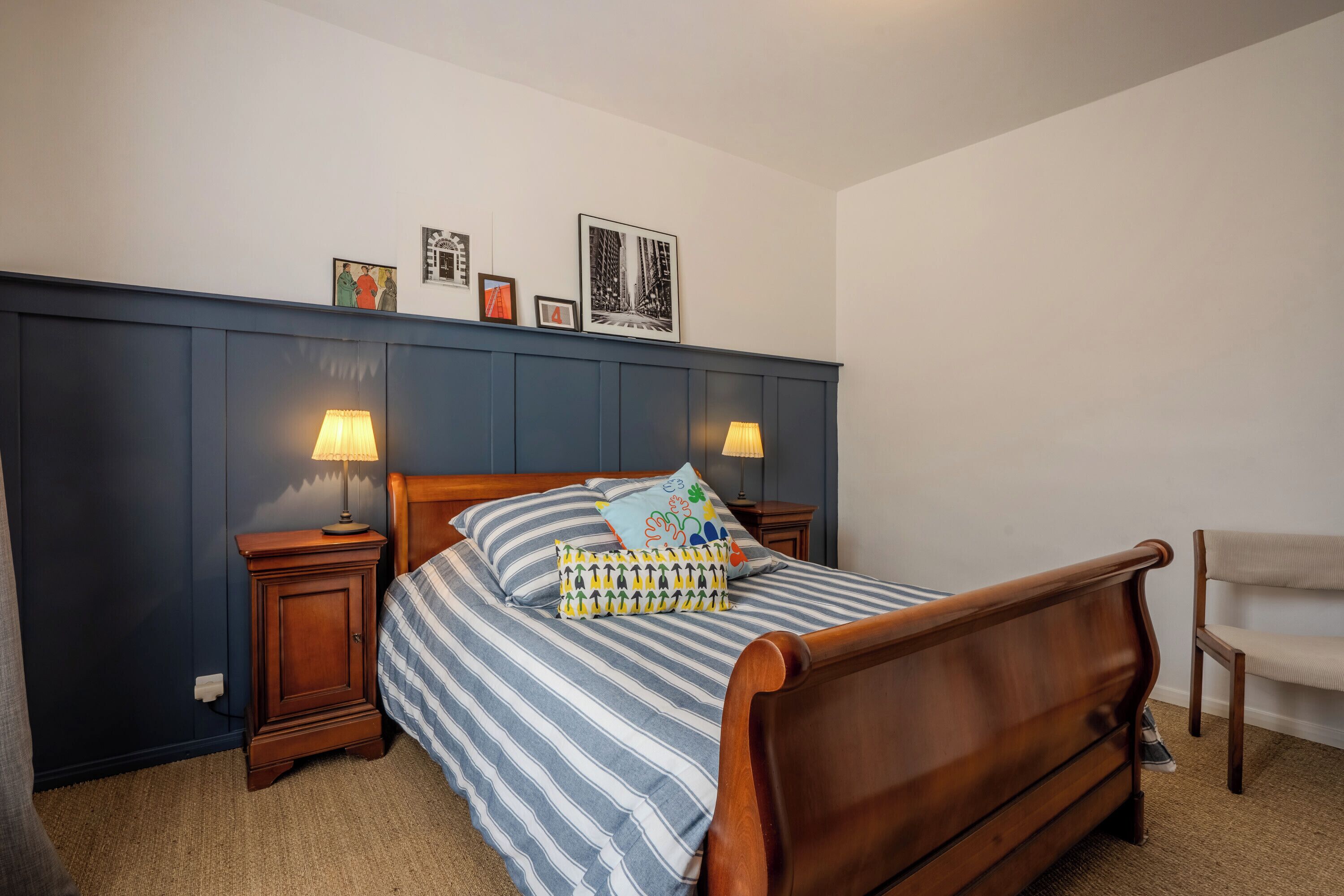 A bedroom with a wooden bed, striped bedding, two bedside tables with lamps, and a chair.
